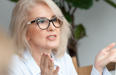 Mature female Travel Manager in glasses speaking at a meeting