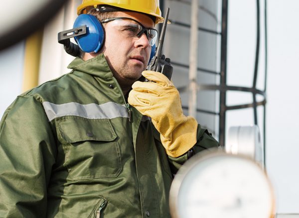 Worker in resource sector wearing PPE and on speaking into a hand-held radio