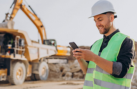 Miner on mine site in hi-vis and hard hat reading CTM's case studies on mobile phone