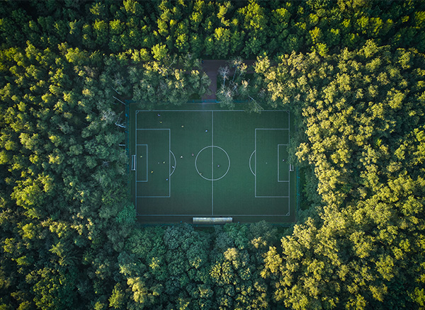 10 Tips for Sustainable Sports Travel Programme - Aerial top down view of football pitch among the forest