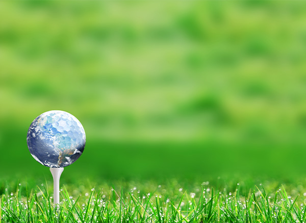 Planet earth golf ball on tee and with defocused bokeh golf course green background and copy space. Concept of eco-friendly golf course